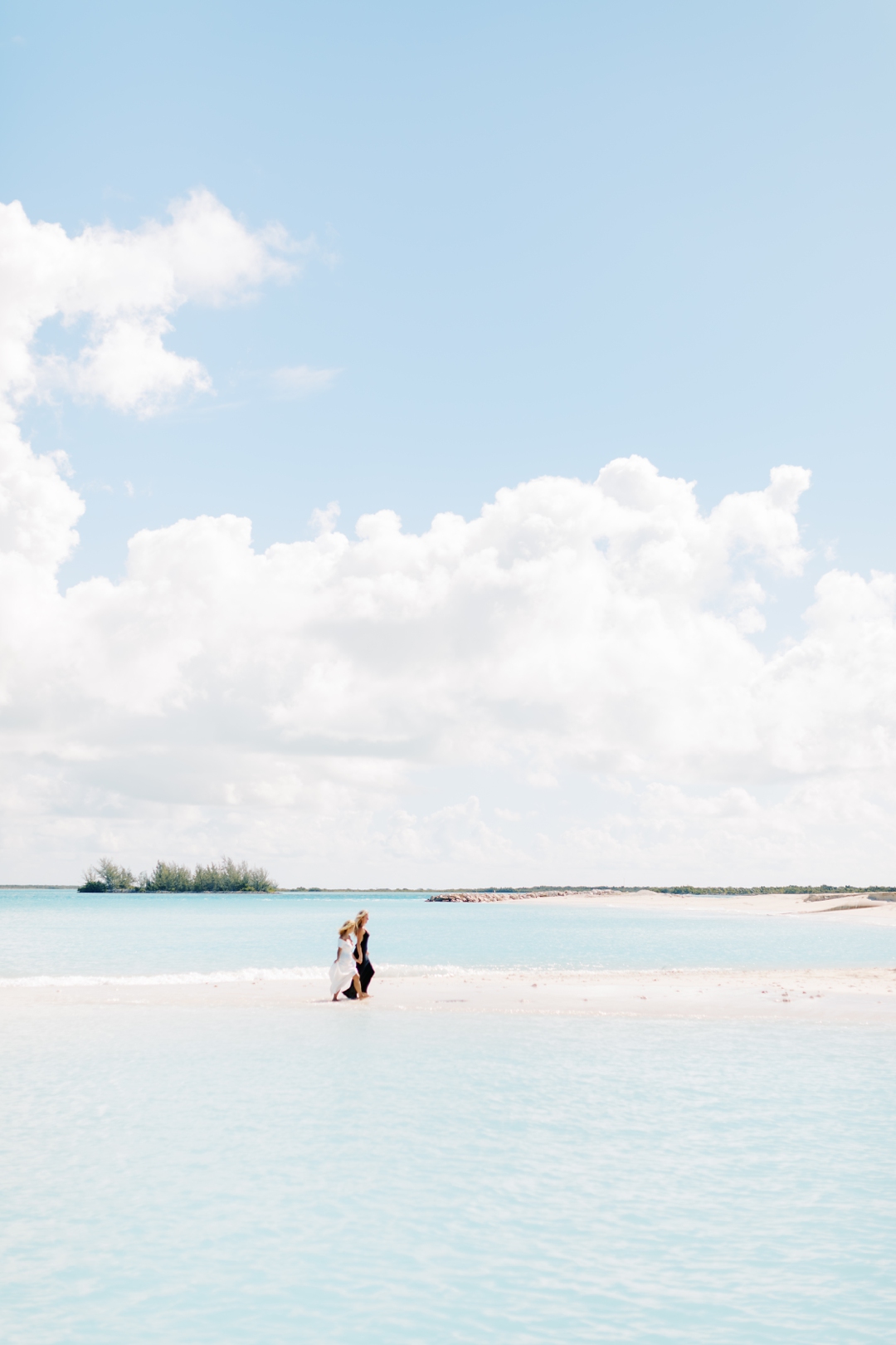 Lesbian Couple holding hands and walking along a turquoise‑water beach