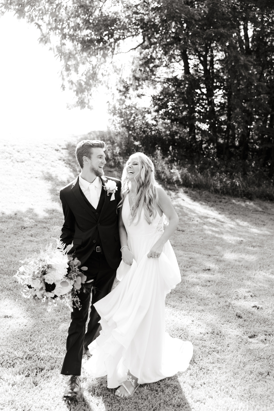 Black‑and‑white portrait of bride and groom laughing together outdoors with greenery