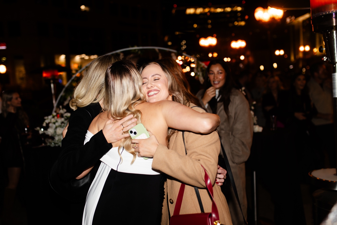 Gracie is hugging a couple of her close friends at the end of her scavenger hunt proposal, looking happy and excited. I think it's really sweet that they are celebrating with their friends and family after the big proposal. I hope they have a long and happy future together.