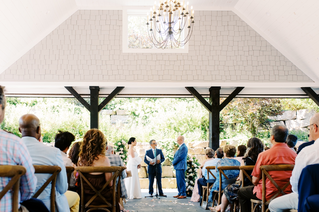 Suzie and Russell exchanging vows on the covered outdoor patio at Sunflower Hill Farm, surrounded by lush floral arrangements.