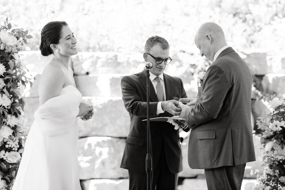 Suzie and Russell exchanging vows on the covered outdoor patio at Sunflower Hill Farm, surrounded by lush floral arrangements.