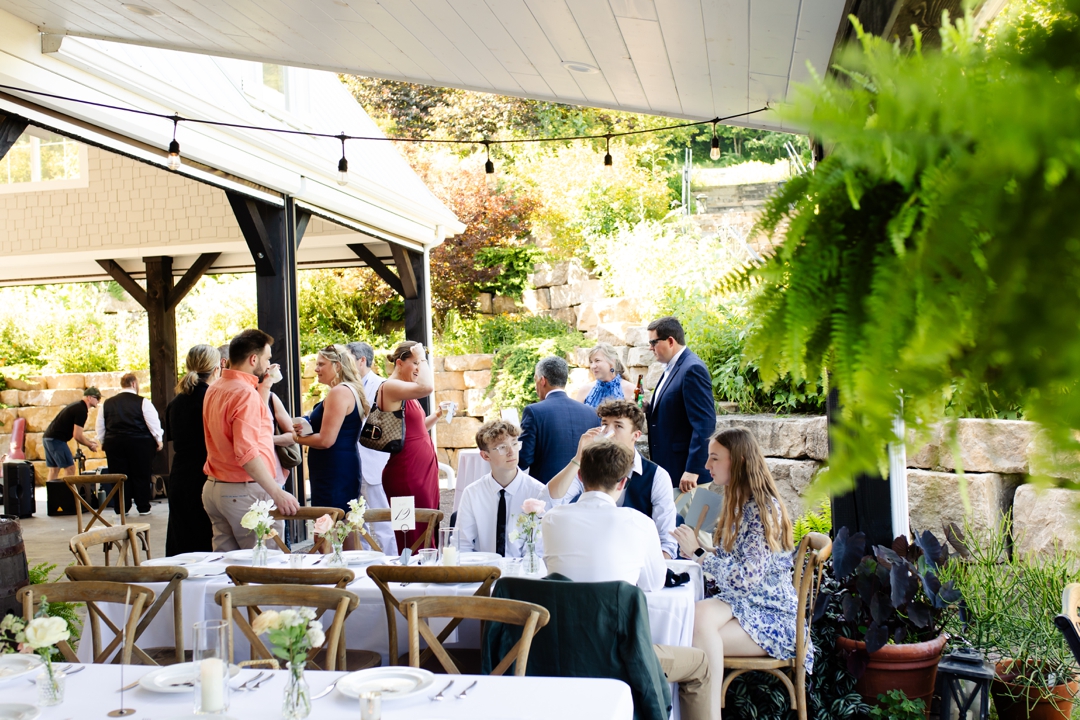 Guests enjoying cocktail hour at Sunflower Hill Farm, mingling under the covered patio with scenic views in the background.