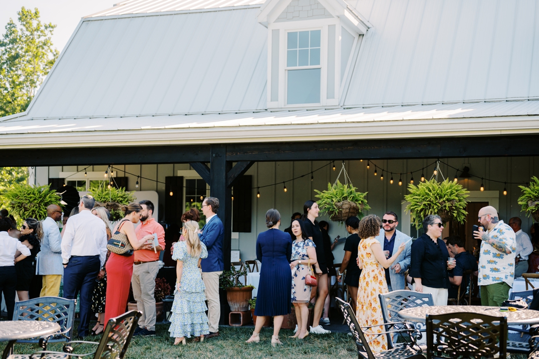 Guests enjoying cocktail hour at Sunflower Hill Farm, mingling under the covered patio with scenic views in the background.