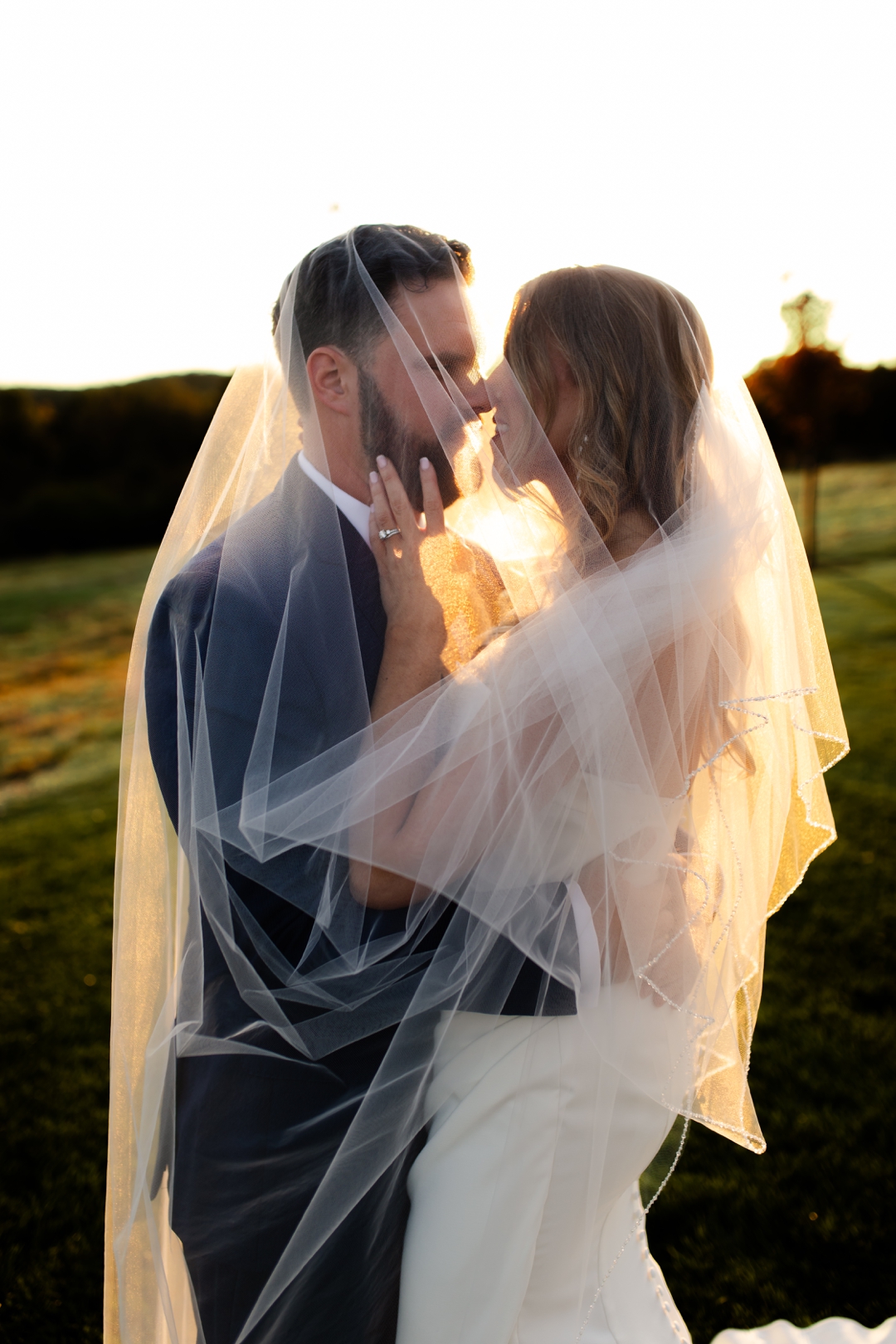 Romantic portrait of bride and groom embracing beneath a translucent veil at sunset