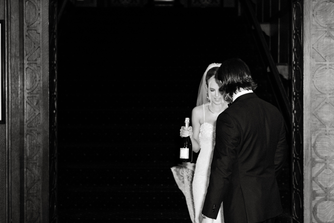 Bride Deane holding the champagne bottle while Jeff helps adjust her dress during their first look.