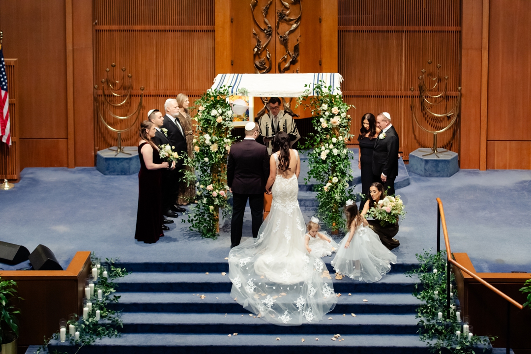 “Allie and Nate standing under a greenery-adorned chuppah at United Hebrew Congregation.