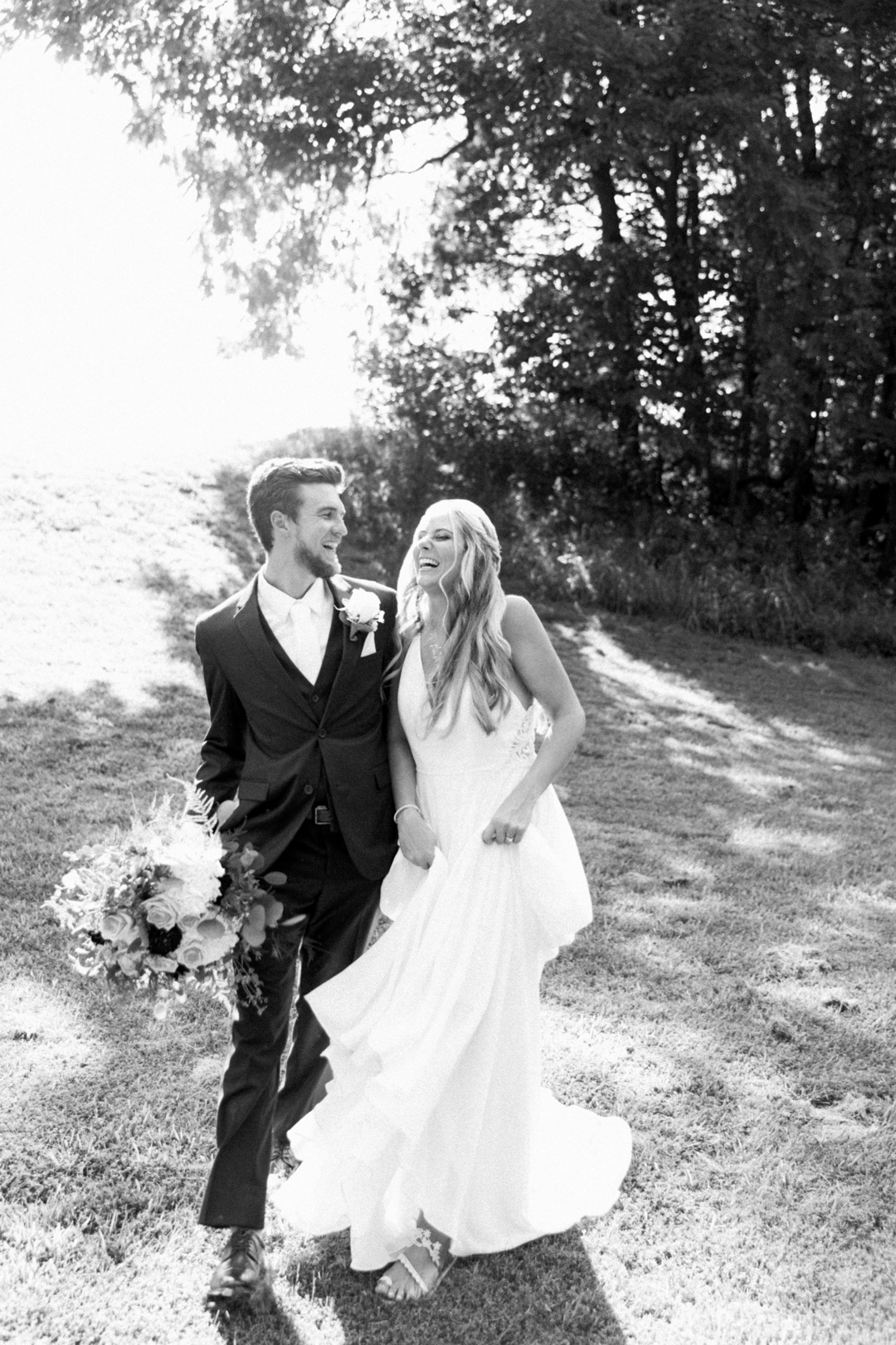 Black‑and‑white portrait of bride and groom laughing together outdoors with greenery
