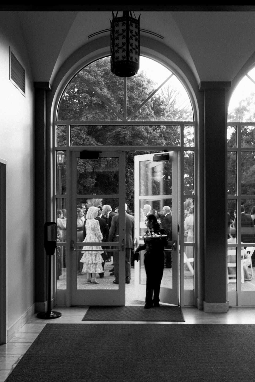 Black and white doorway scene with wedding guests gathered outside, framed like a cinematic still