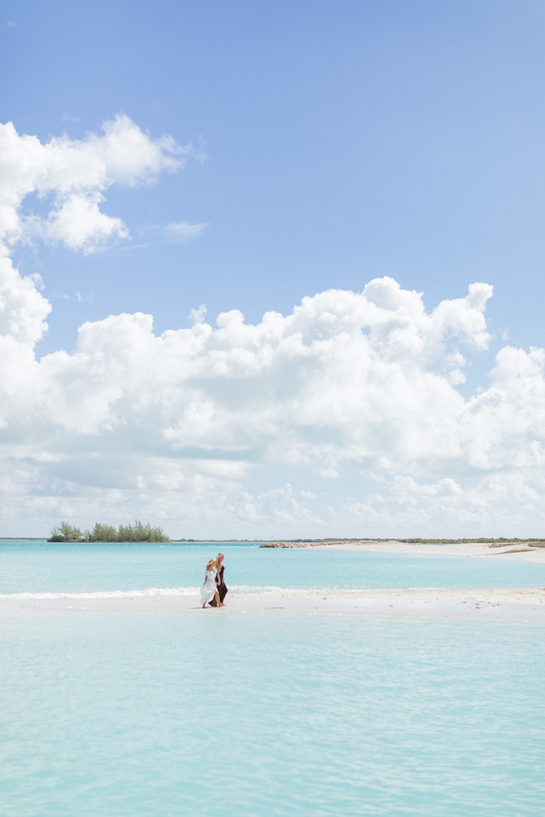 Lesbian Couple holding hands and walking along a turquoise‑water beach