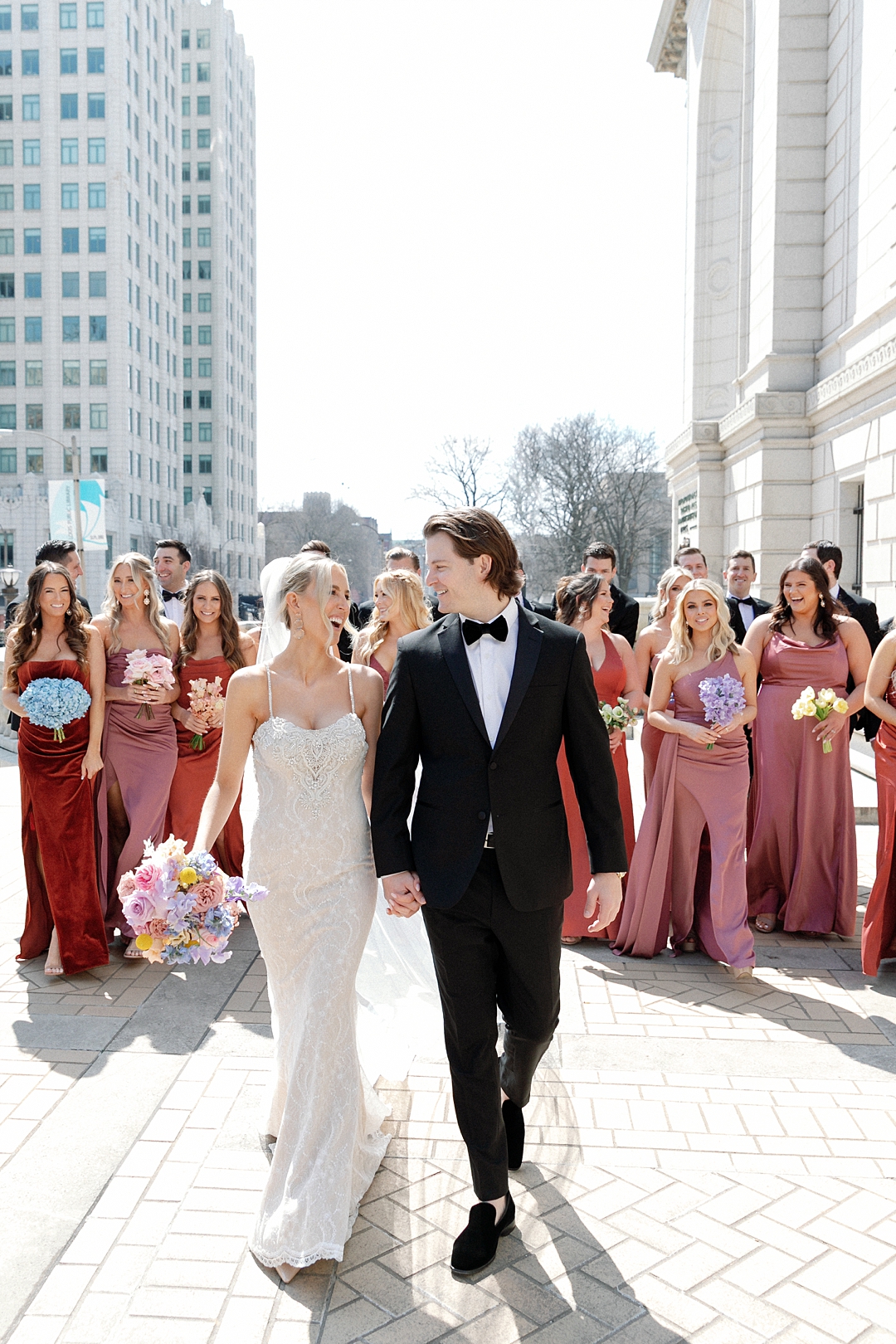 bride and groom walking with wedding party in background in downtown st louis