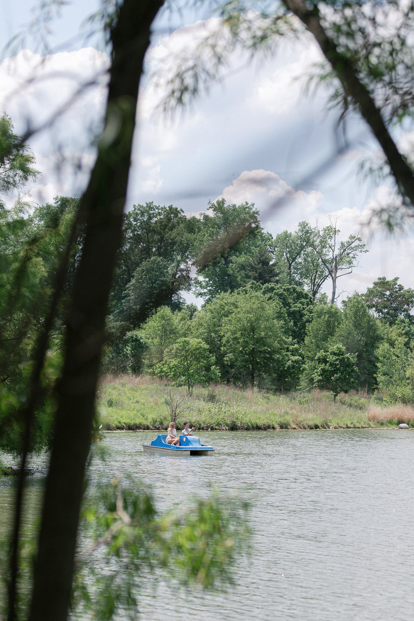 Wide view of couple on a paddle boat in Forest Park FaceTiming family after the proposal