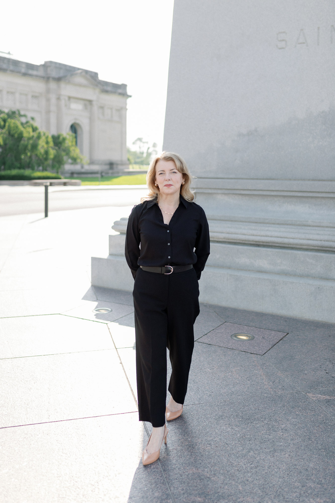 Full length outdoor professional headshot of a woman standing near architectural stone wall in St. Louis