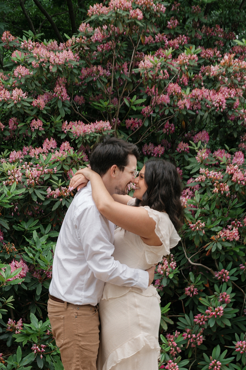 Elise and Hayden kissing in front of pink flowers during their engagement session