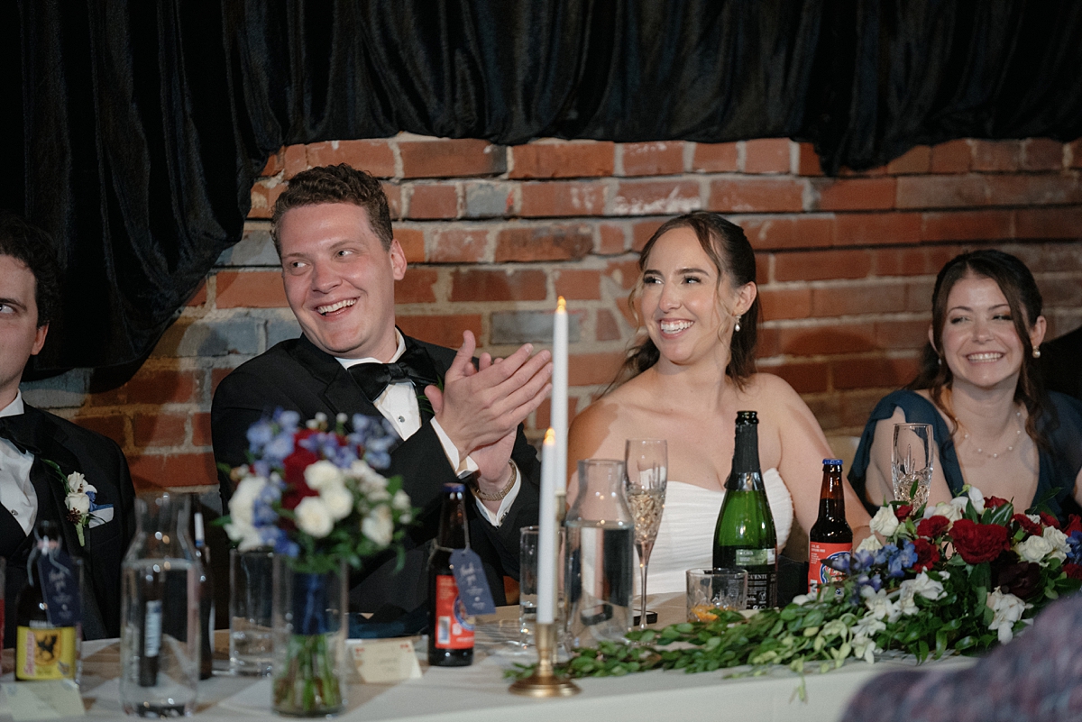 Jill and Dylan smiling during speeches at their St. Louis wedding reception