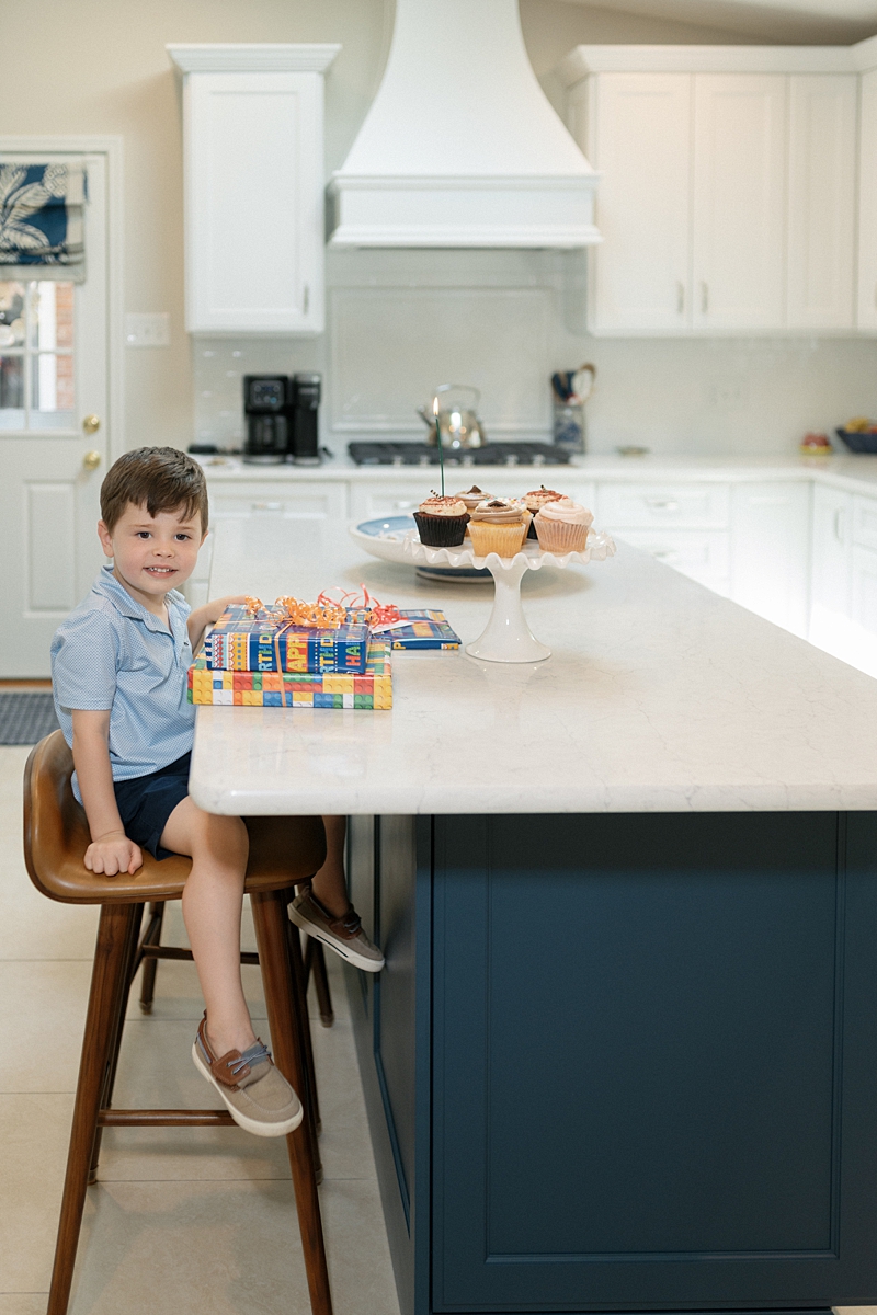 Young boy sitting at a kitchen island with cupcakes and birthday gifts