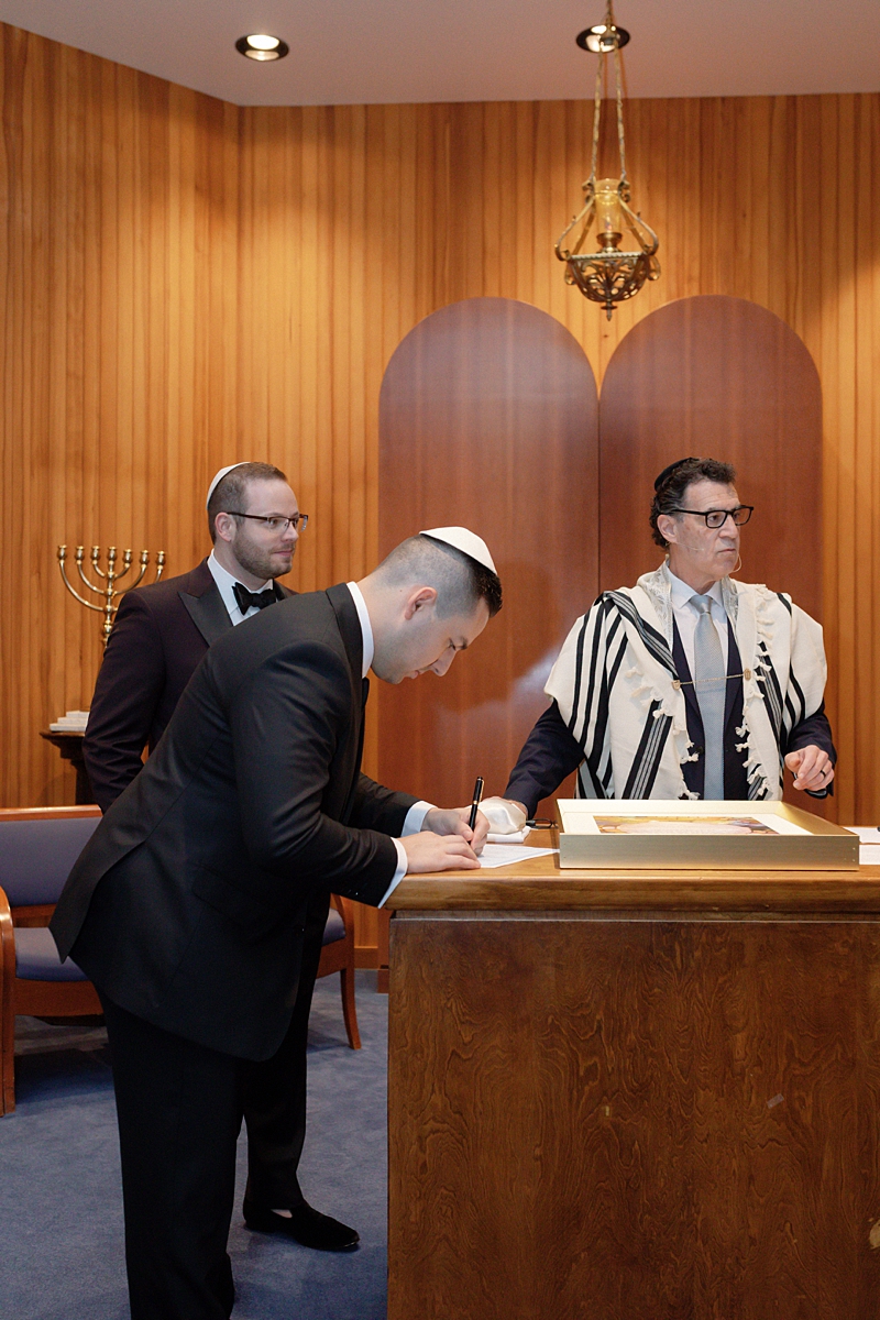 A signature at the ketubah table with the officiant nearby