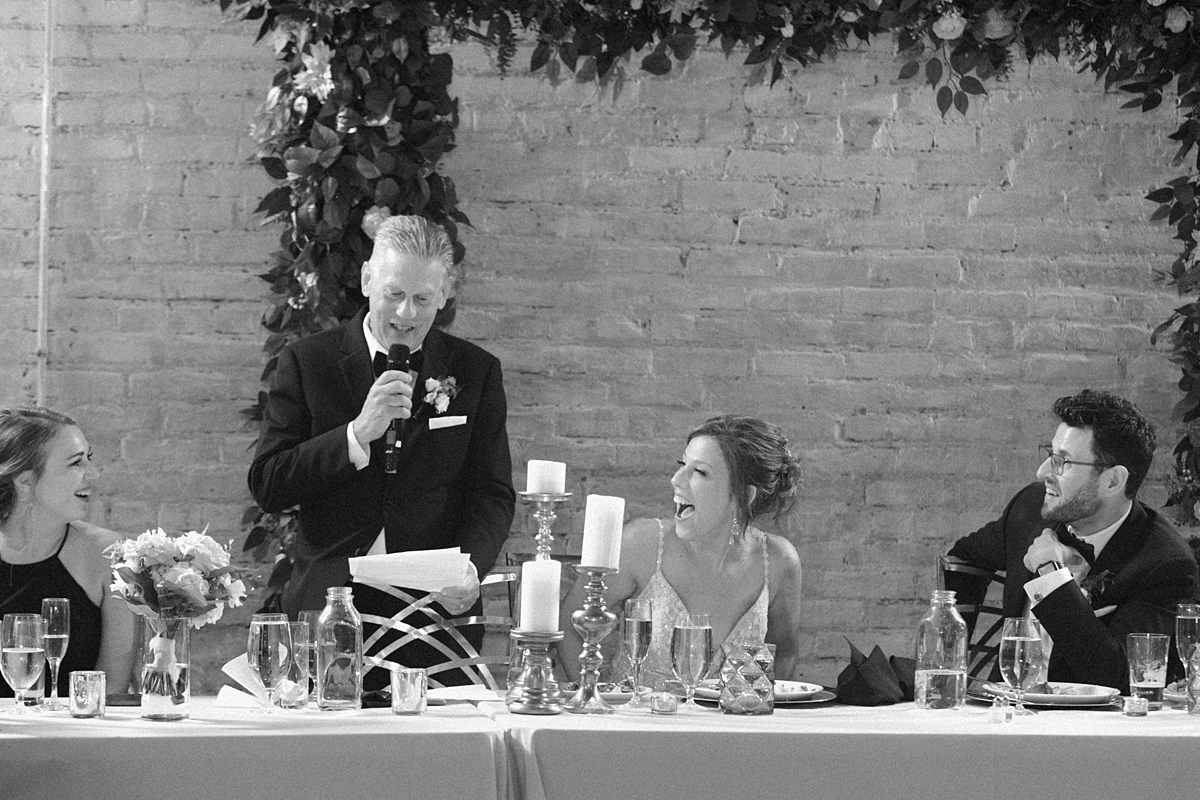 Black and white wedding speech photograph showing Lauren and Nick laughing at their reception