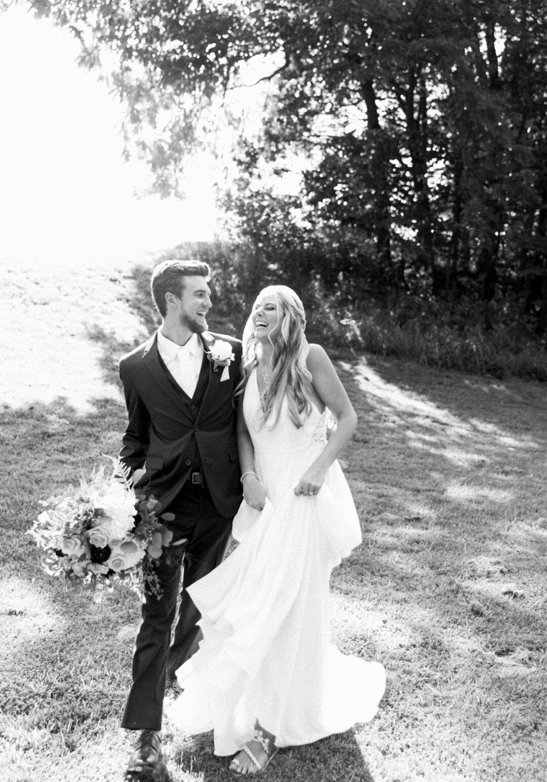 Black‑and‑white portrait of bride and groom laughing together outdoors with greenery